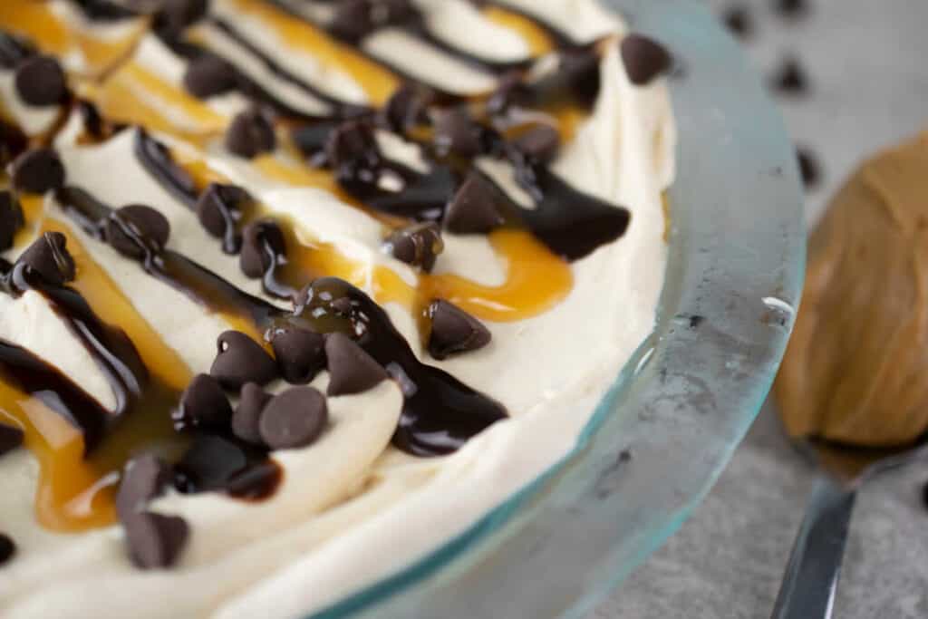 Peanut butter pie topped with whipped cream and chocolate chips and drizzled with chocolate.