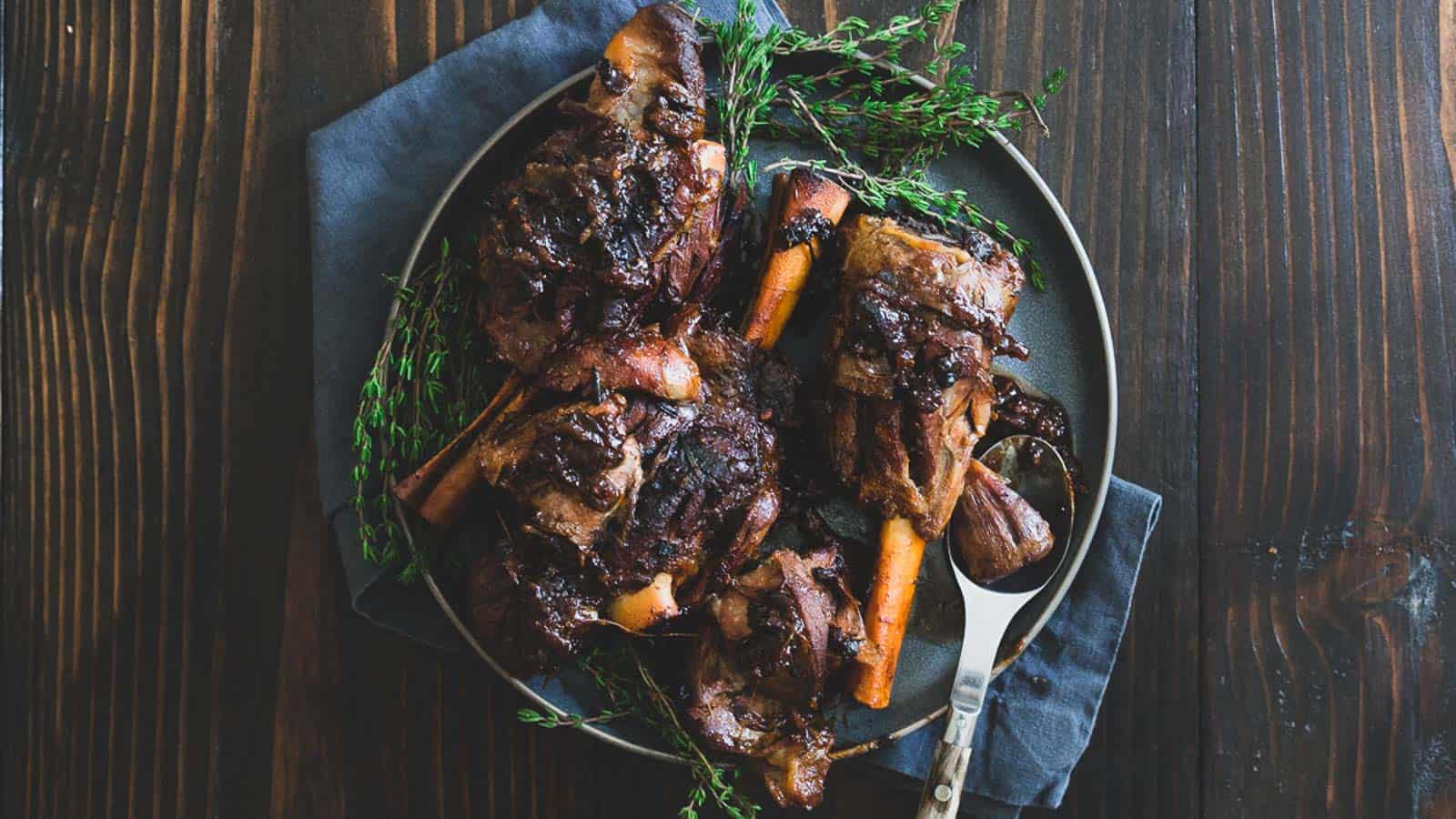 Apple cider braised lamb shanks on a gray plate with fresh thyme sprigs.