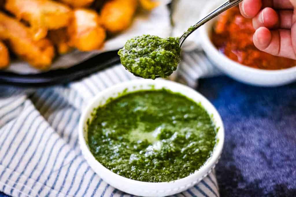 High angle shot of a bowl of cilantro mint chutney with a spoonful being lifted above the bowl.