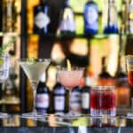 Five cocktails in different glasses on a bar.