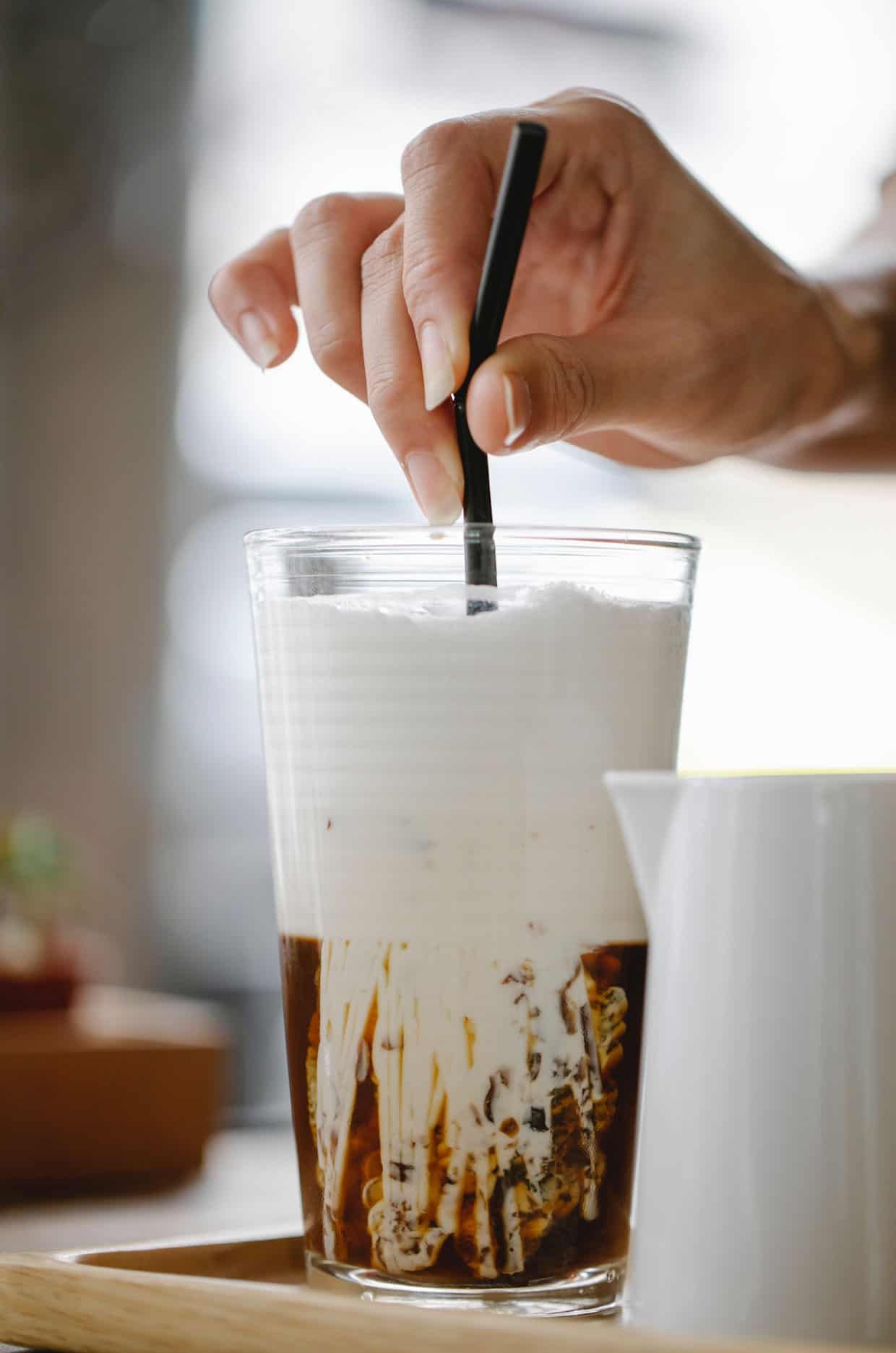 Stirring cold foam into iced coffee glass.