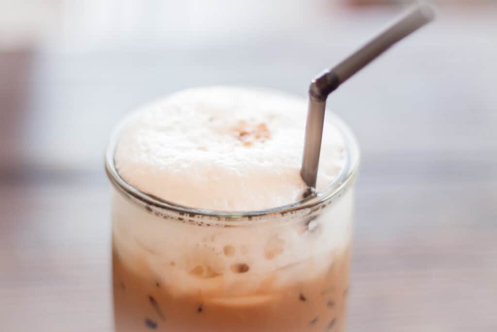 Cold foam on top of iced coffee in a glass with a metal straw.