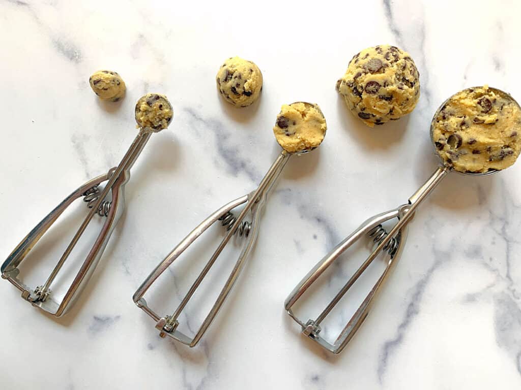 Three cookie scoops filled with cookie dough.