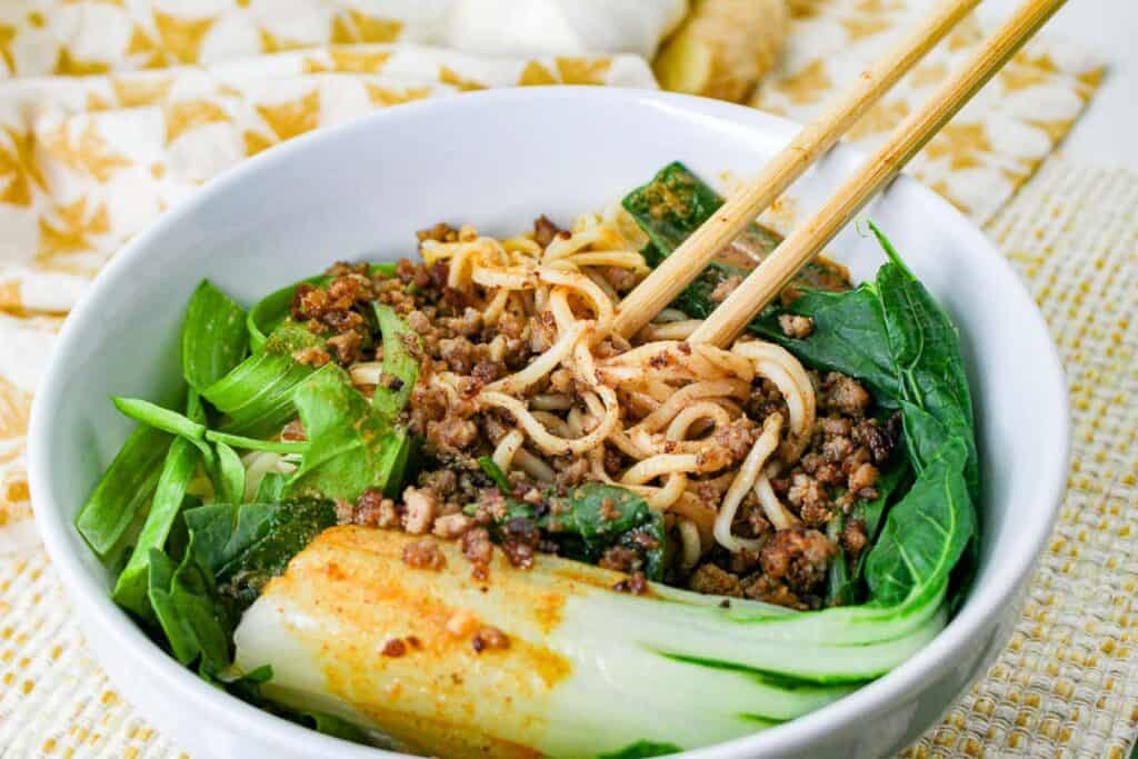 Dan dan noodles with bok choy in a white bowl with chopsticks.