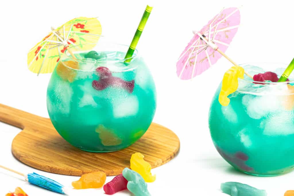 a blue cocktail with candy fish in the drink and a cocktail umbrella on top.