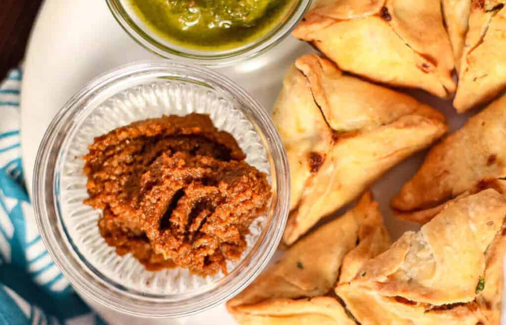 Overhead shot of garlic chutney in a bowl with a plate of samosas.