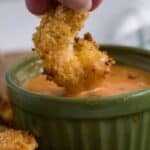 A person dipping fried shrimp into a bowl of dip.