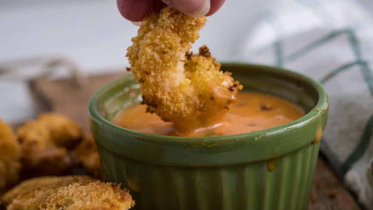 A person dipping fried shrimp into a bowl of dip.