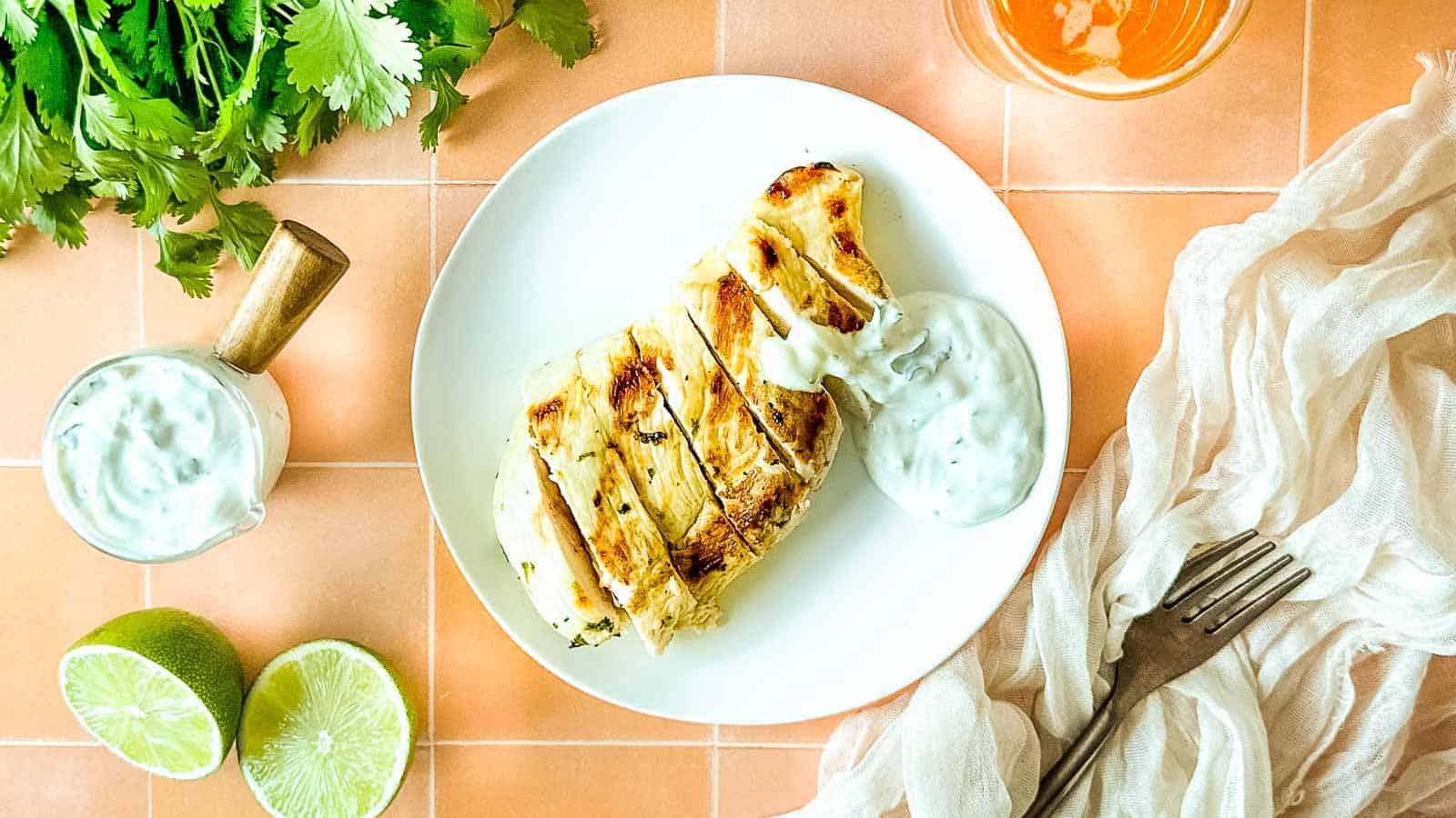 Grilled, sliced chicken on a white plate with cilantro crema.