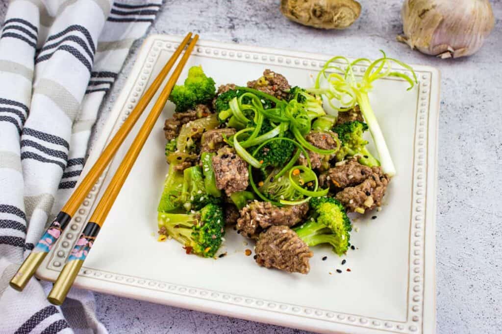 Square plate with ground beef and broccoli along with chopsticks.