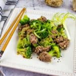 Square plate with ground beef and broccoli along with chopsticks.