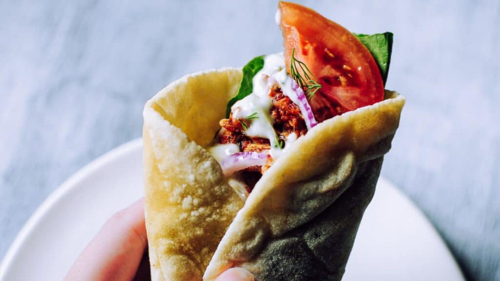 A hand holding veggies wrapped in pita bread.