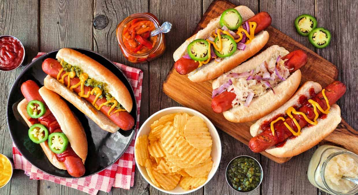 top view of assorted hot dogs in buns with different toppings like mustard, relish, jalapenos.
