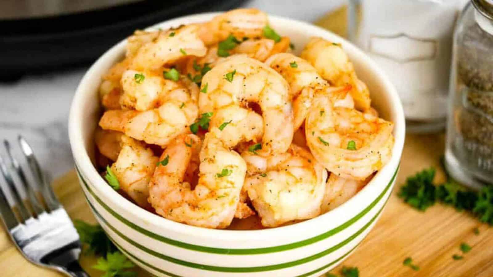 Cooked shrimp in a green and white striped bowl, garnished with parsley.