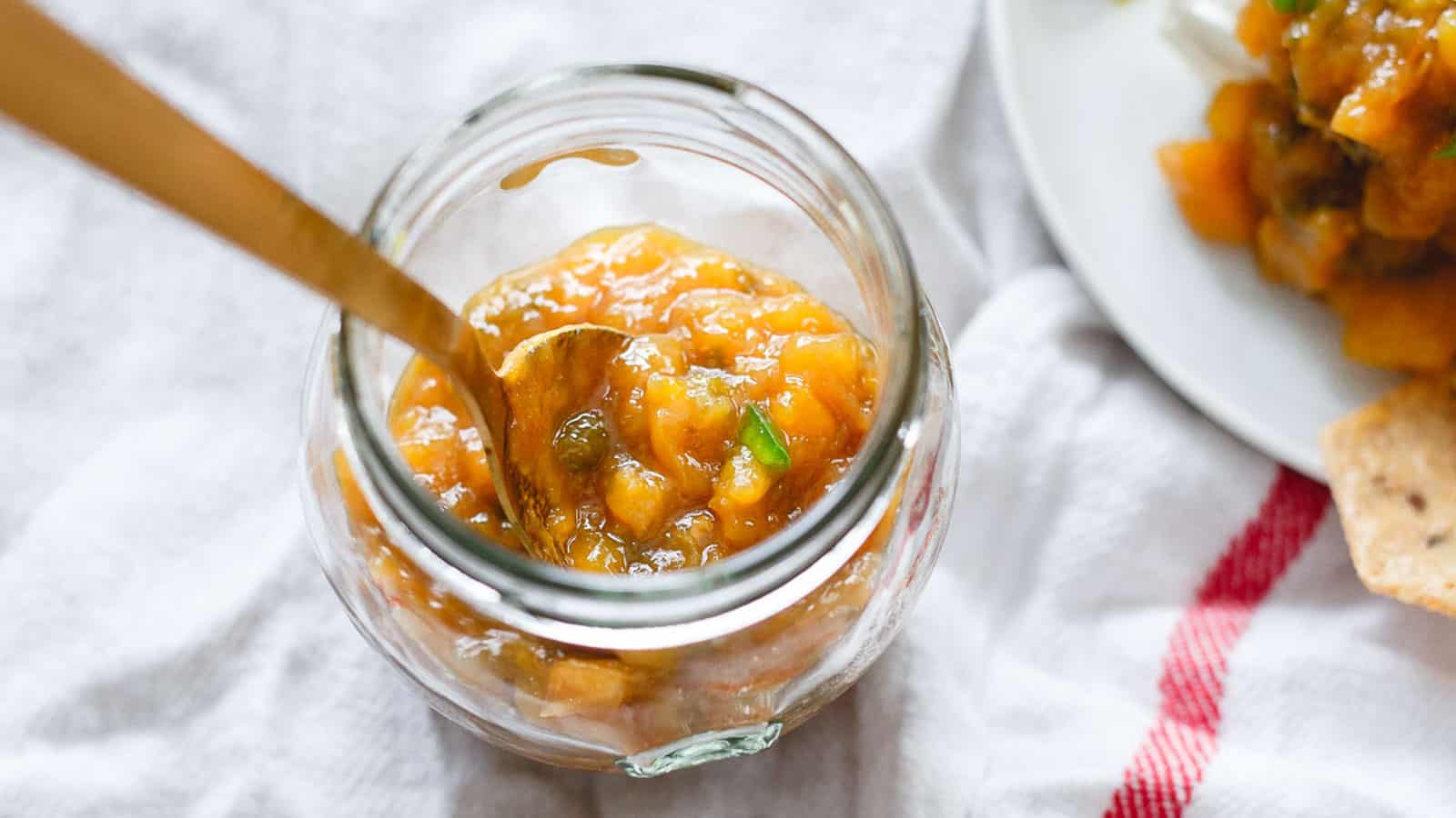 Jalapeño mango jam in a glass jar with a spoon.