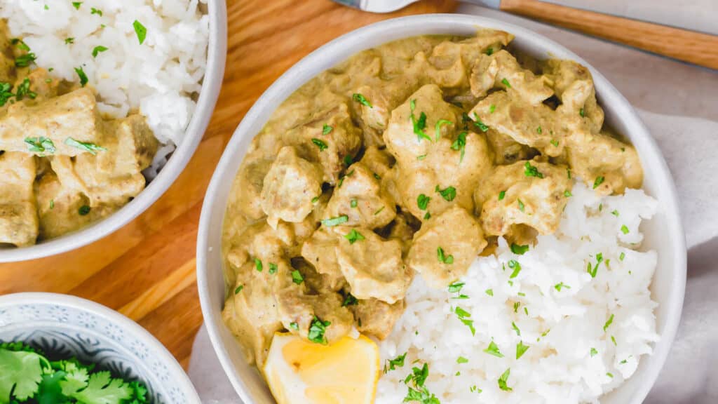 Lamb korma in a bowl with white rice and lemon wedge.