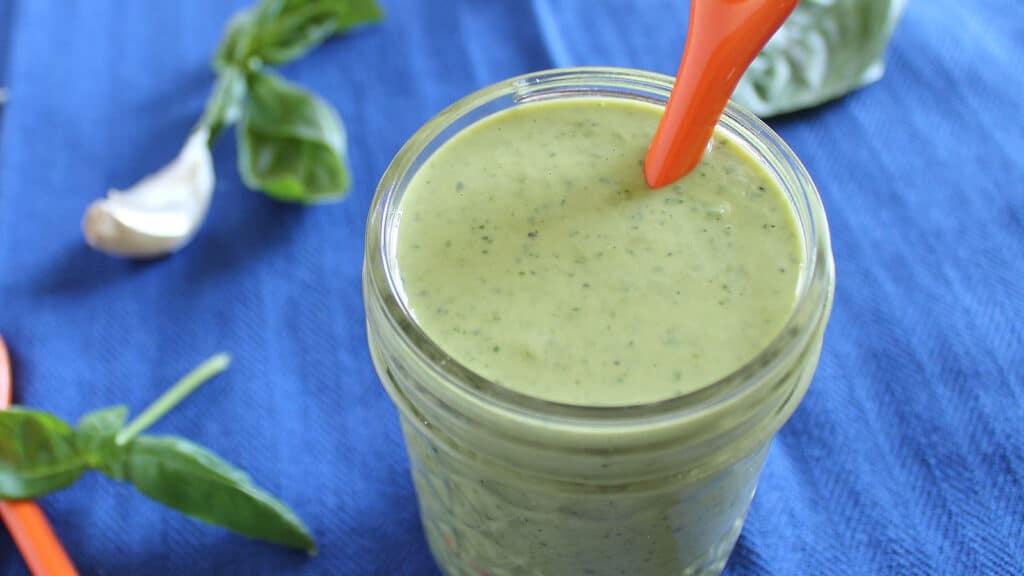 Garlic lemon herb tahini dressing in a glass jar with an orange spoon.