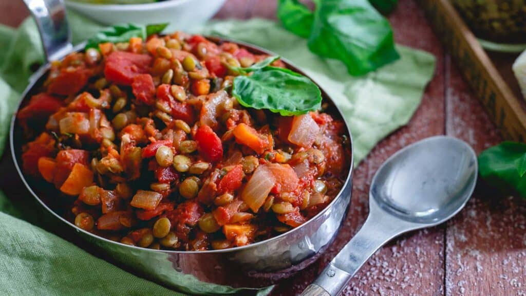 Lentil bolognese garnished with basil in a metal dish.