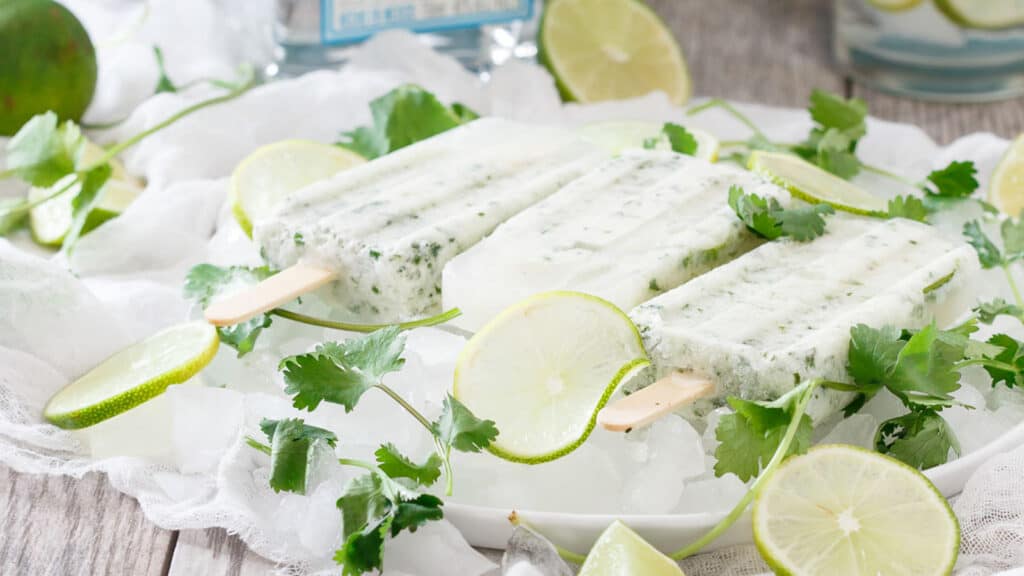 Margarita ice pops on ice with lime slices and cilantro.