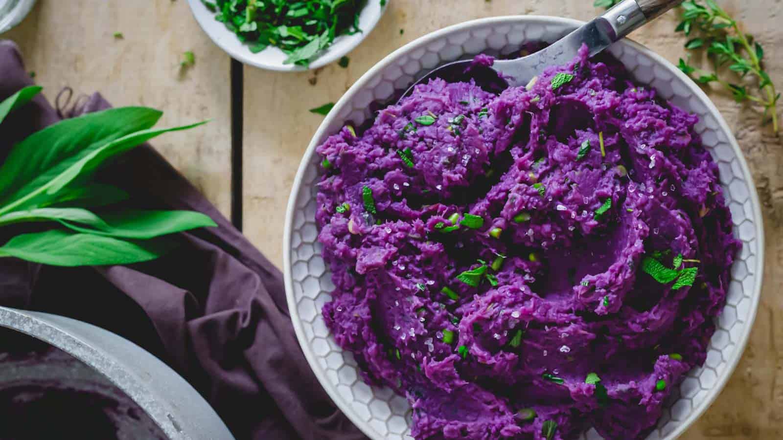 Mashed purple sweet potatoes in a bowl with a serving spoon.