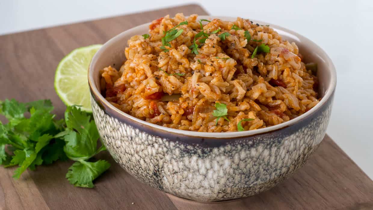 Brown bowl with Mexican rice on a wooden cutting board with cilantro and lime.