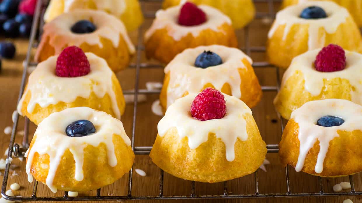 Mini lemon bundt cakes on a cool rack drizzled with icing and topped with raspberries and blueberries.