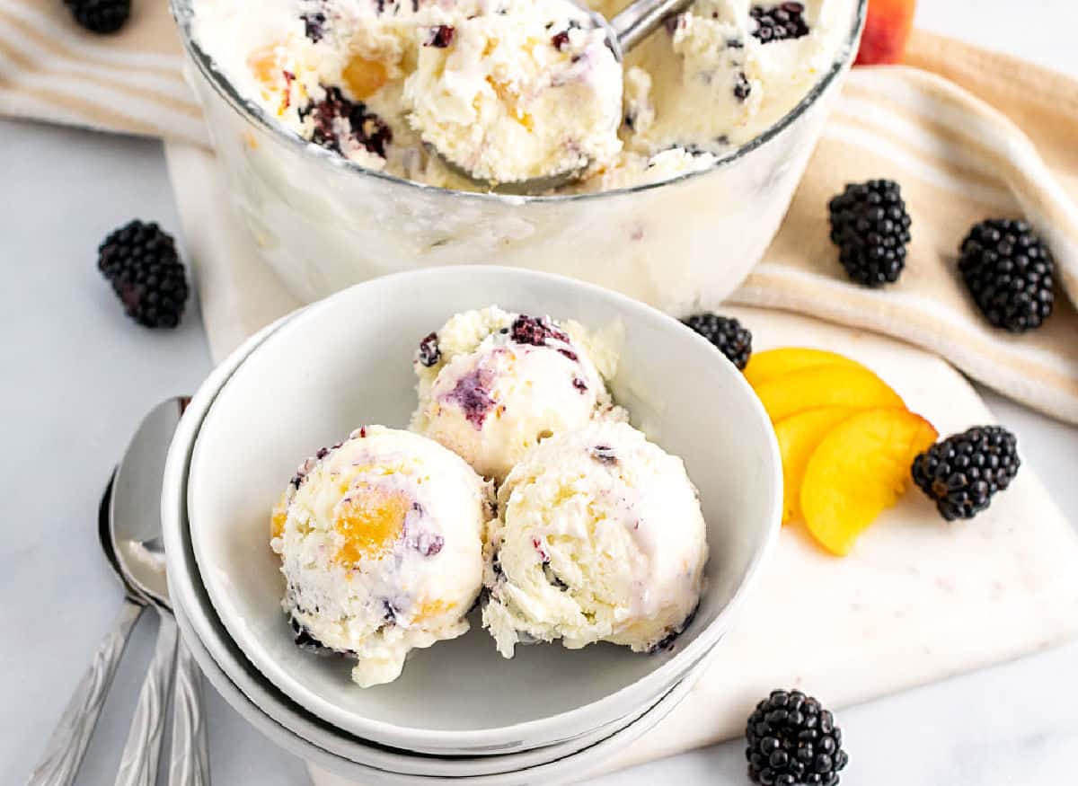 Peach and blackberry ice cream scoops in white bowls.