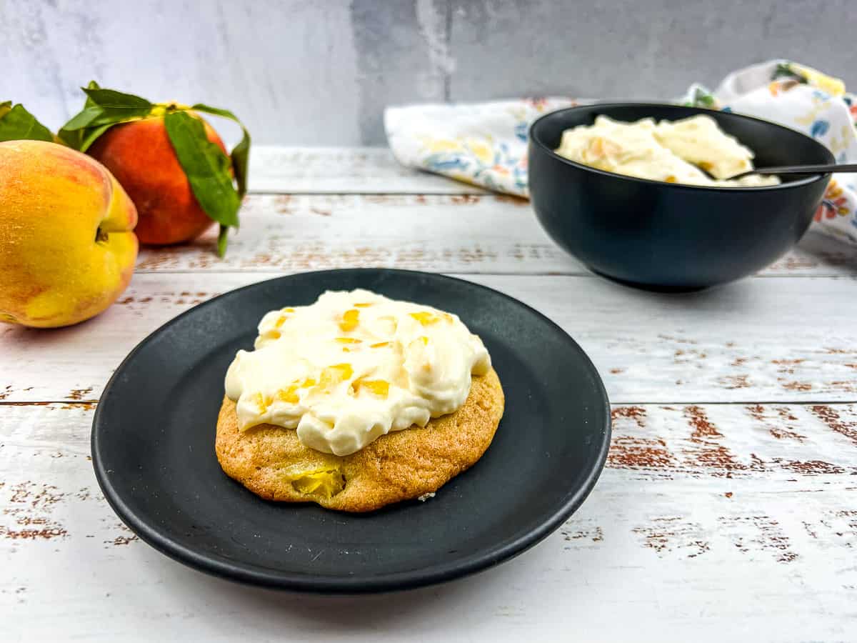 Peaches and cream cookies on a plate with fresh peaches nearby.