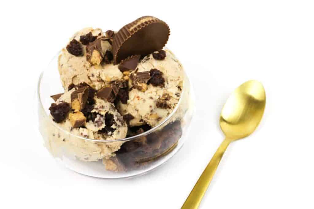 Glass bowl with peanut butter brownie ice cream next to a spoon.