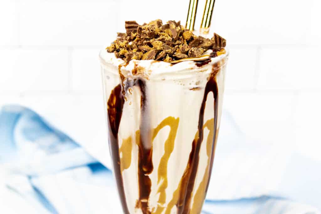 Glass with milkshake with peanut butter and chocolate drizzle topped with diced peanut butter cups.