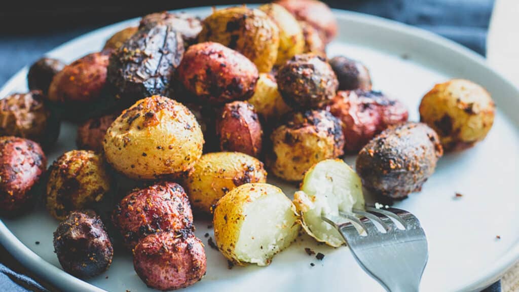 Roasted peri peri baby potatoes on a white plate with a fork.