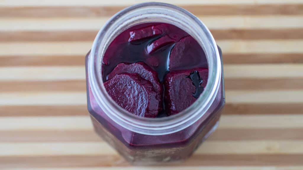 Top view of a jar of pickled beets on a wooden cutting board.