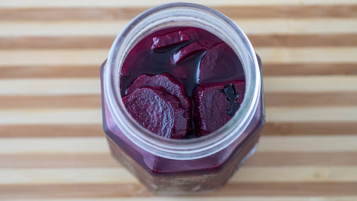 Top view of a jar of pickled beets on a wooden cutting board.