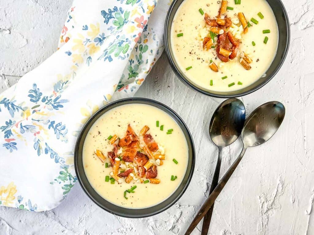 Potato Bacon Cheddar Soup in 2 black bowls with spoons nearby.