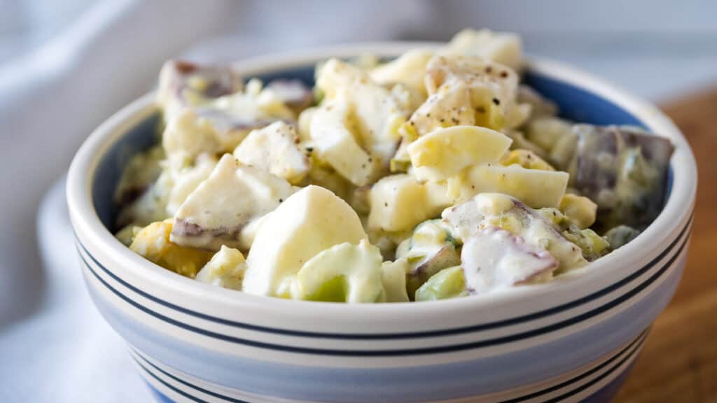 Potato and egg salad in a blue striped bowl.