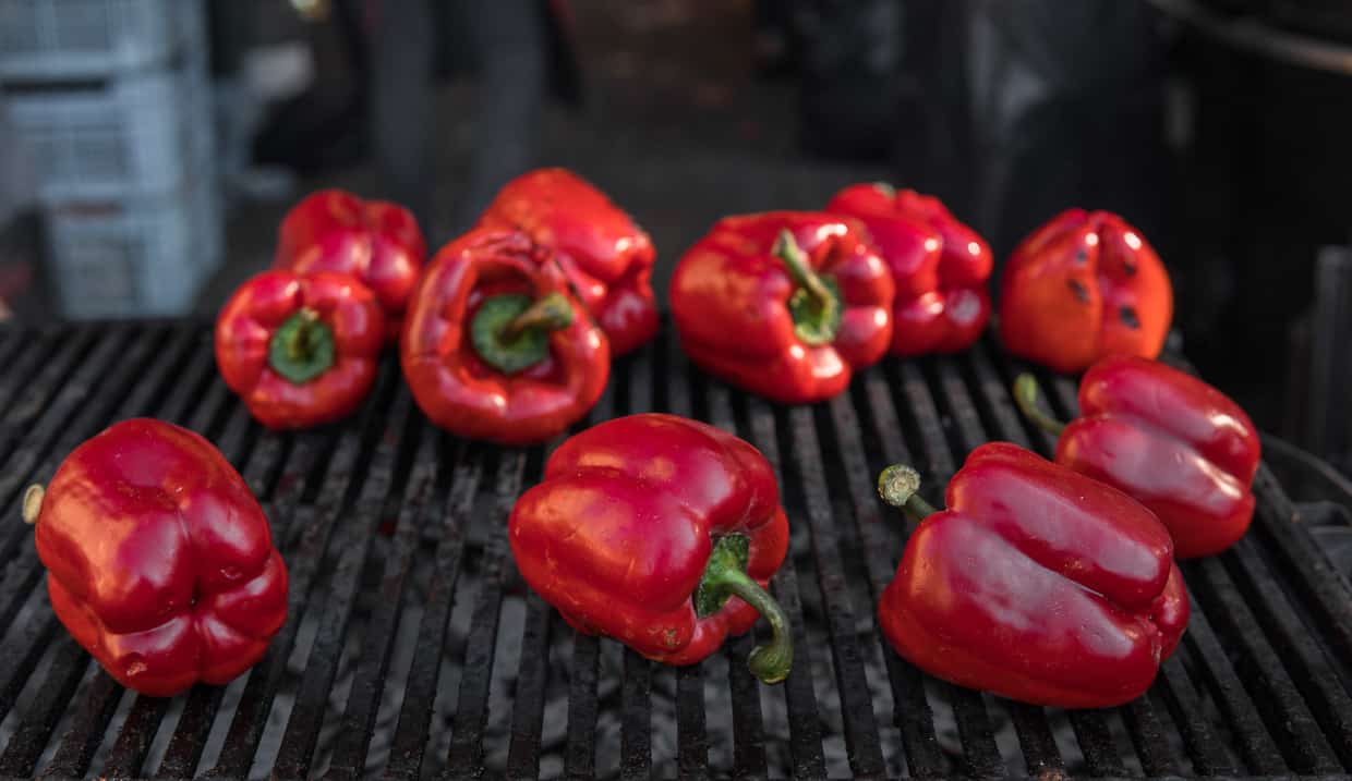 Red peppers roasting on a grate over a gas flame. 