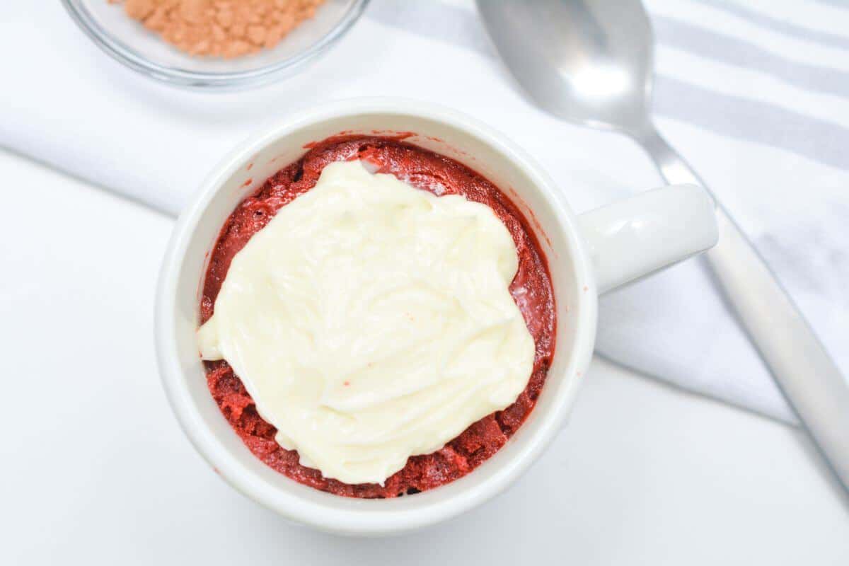 Overhead view of a frosted red velvet mug cake.