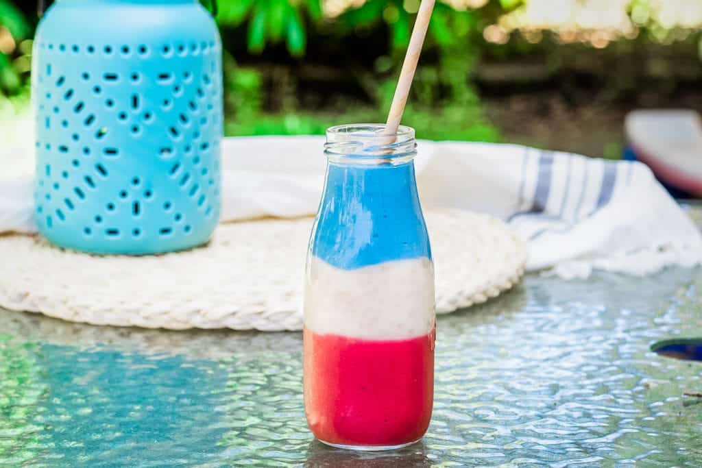 Glass with layered red, white and blue smoothie on a table.