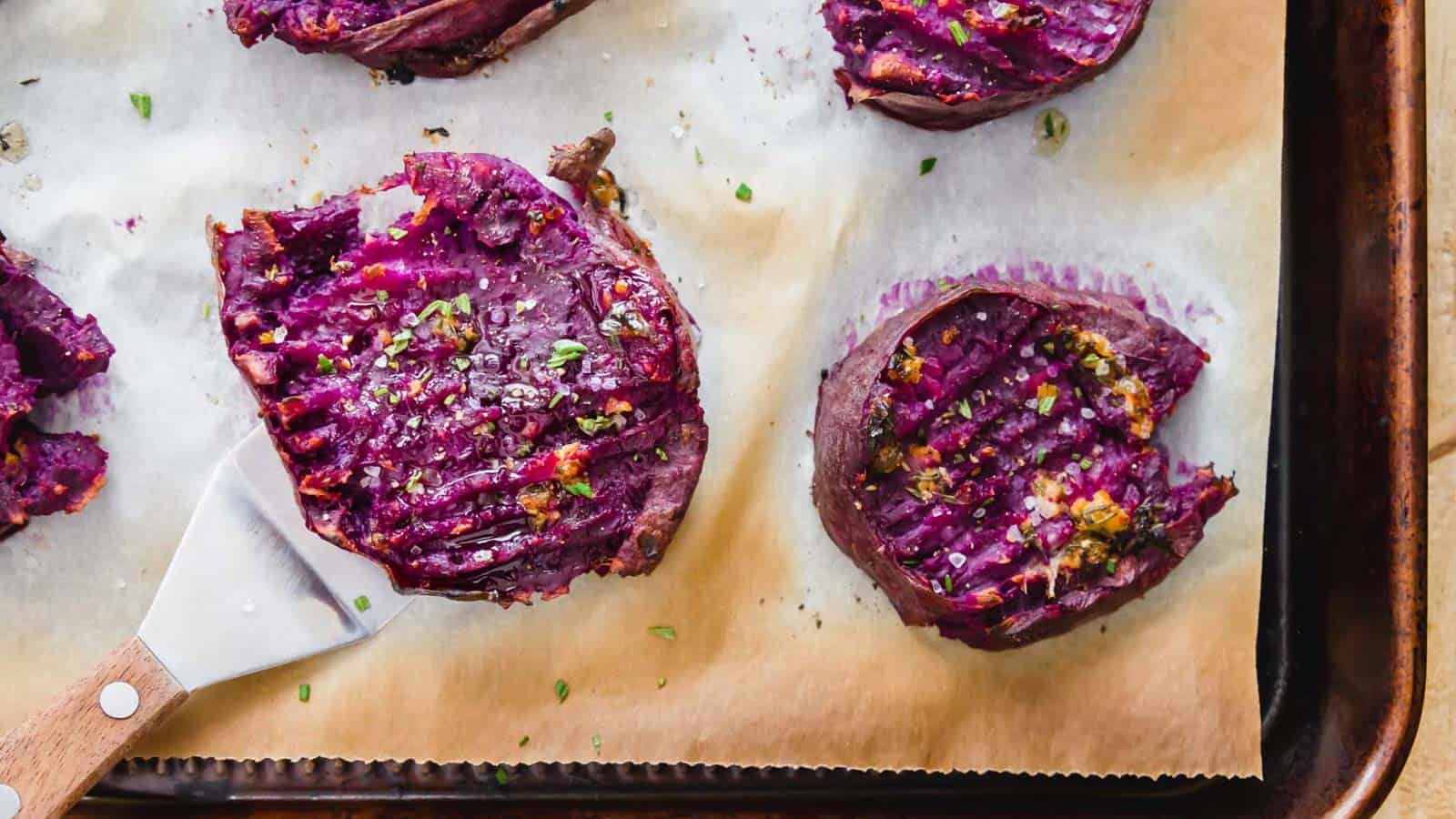 Smashed roasted purple sweet potatoes on parchment paper lined baking sheet.