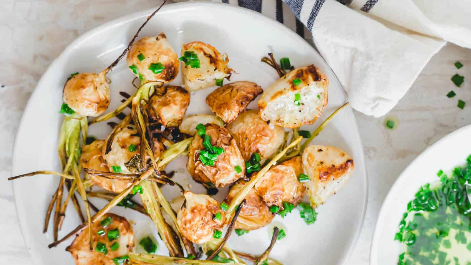 Crispy roasted turnips with chive butter sauce on a white plate.