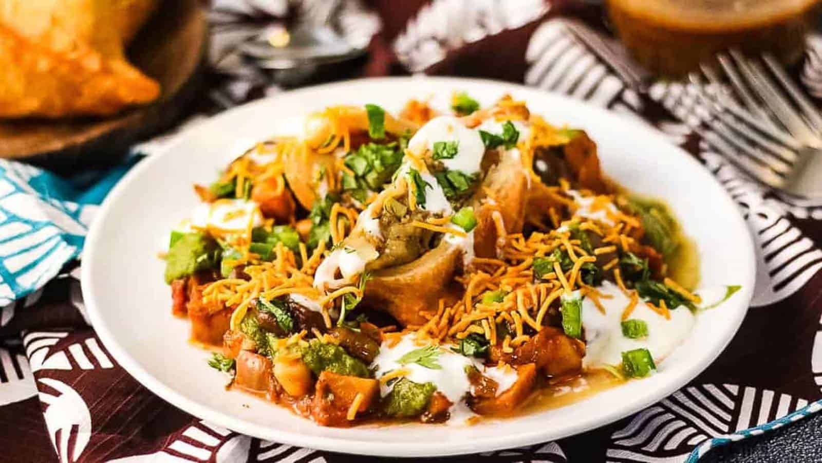 Samosa chaat on a white plate with a brown and white napkin underneat.