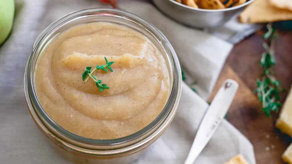 Apple thyme butter in a glass jar garnished with thyme leaves.