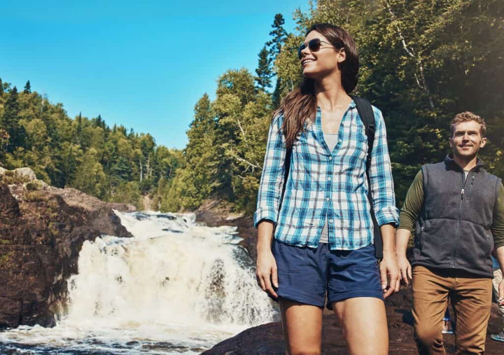 A Young Couple Walking Next To A Rocky River And Waterfall.