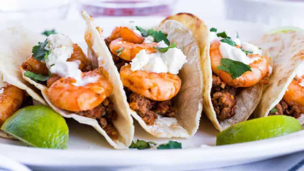 Low angle shot of shrimp and chorizo tacos with lime wedges.