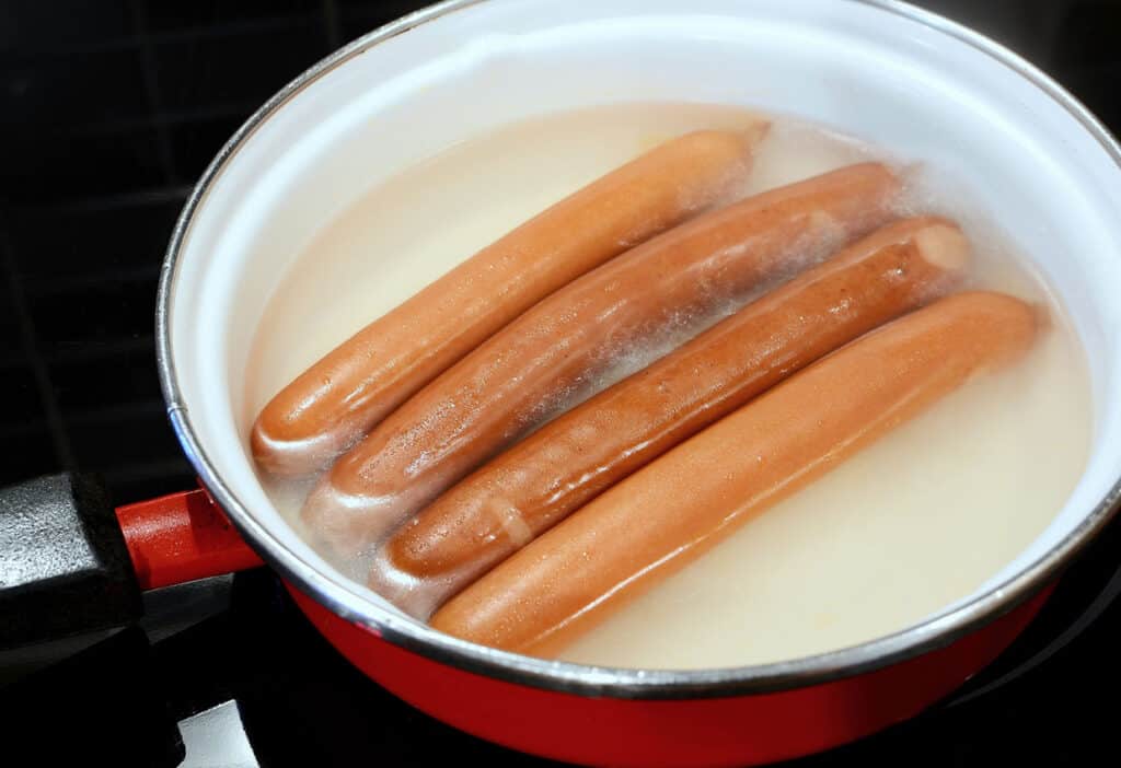 cooking hot dogs in simmering pot of water.