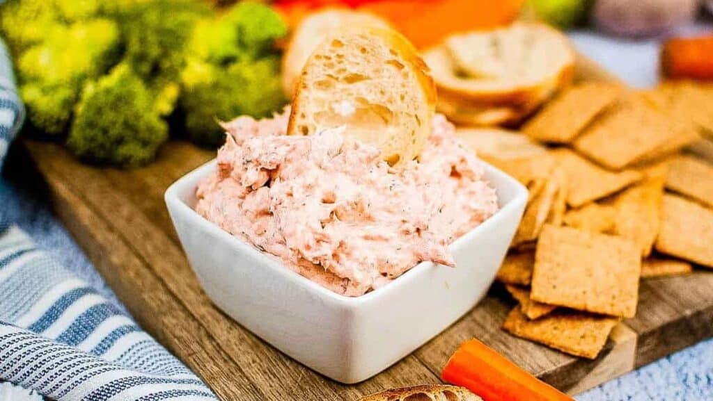 Smoked salon dip in a white bowl with crackers and veggies for dipping.