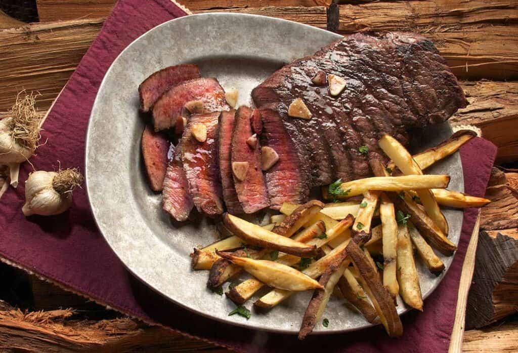 Steak partially sliced with fries on a metal platter.