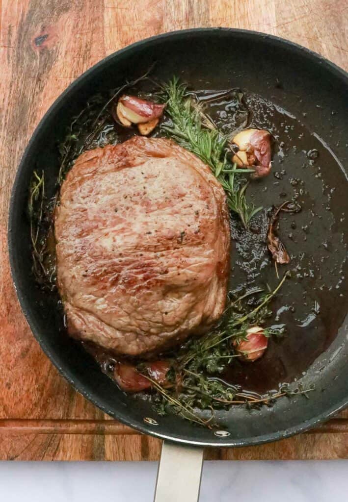 Steak with rosemary and garlic in skillet.