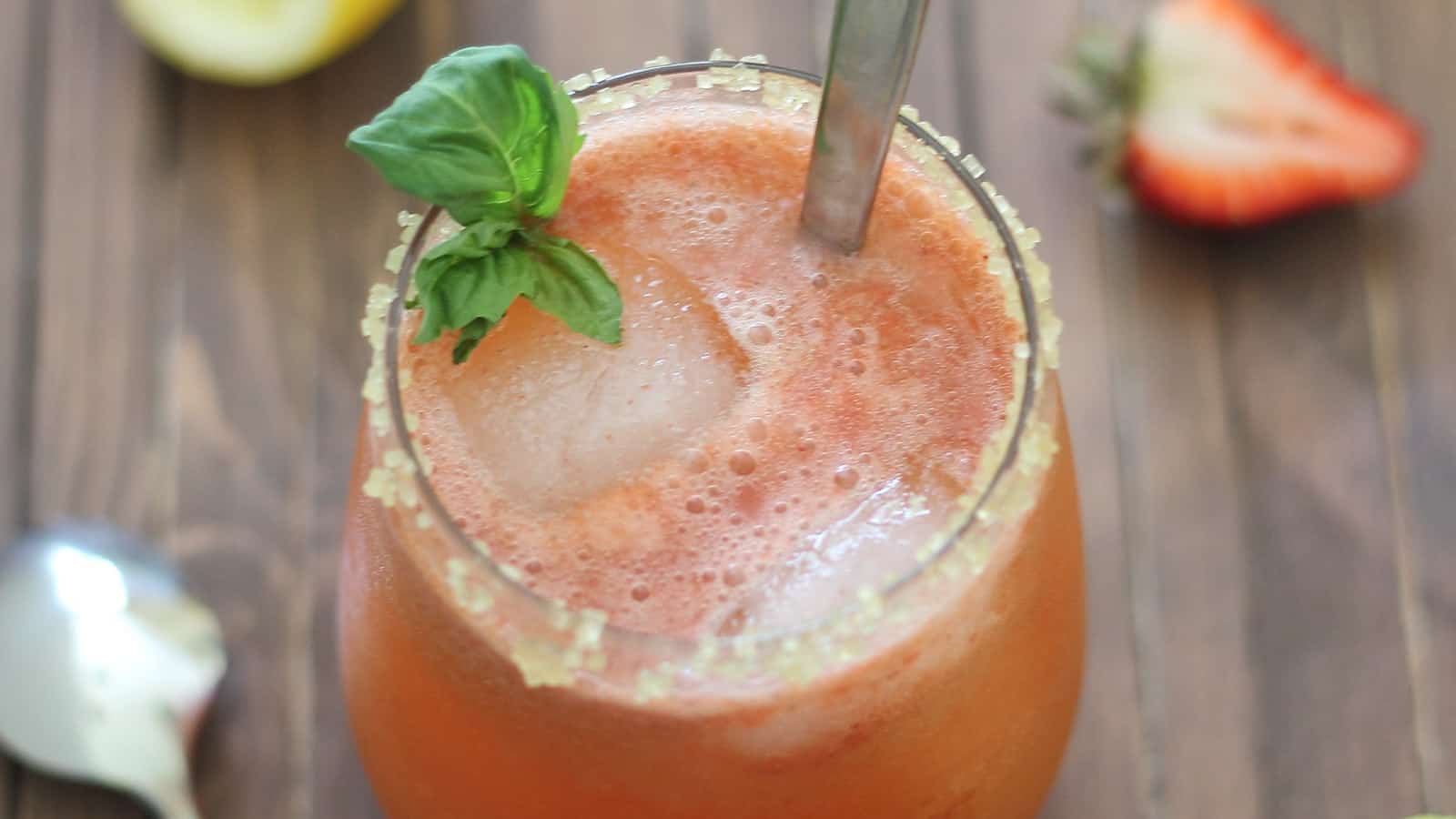 Strawberry basil lemonade in a glass with ice cubes, mint garnish and a spoon.