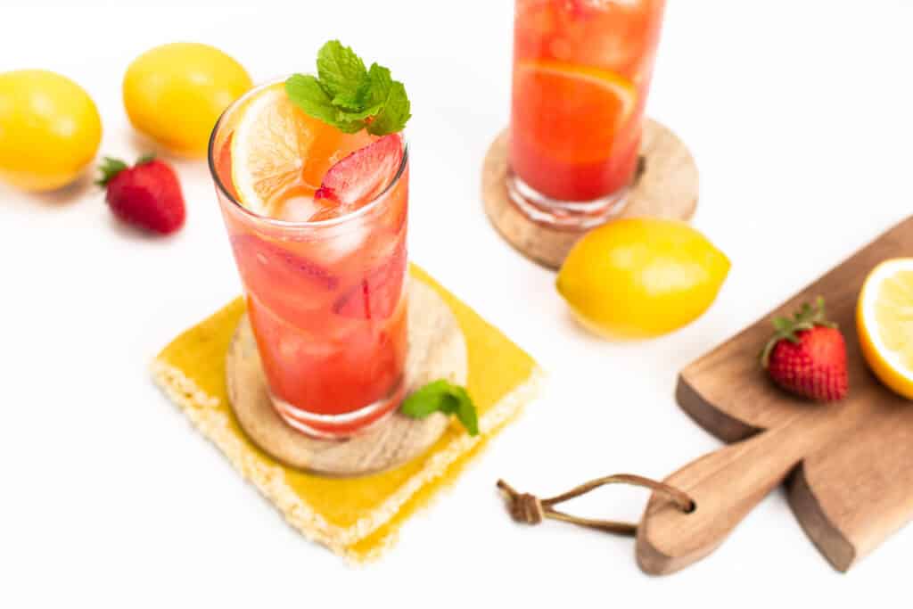 mint leaves, strawberries and lemon slices garnish a glass of strawberry lemonade.